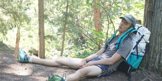 Exhausted man leaning against tree trunk on hike