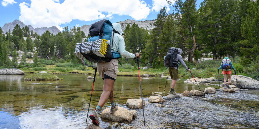 3 backpackers crossing mountain stream