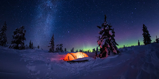 Long exposure image; glowing orange tent under stars and Northern lights